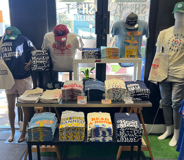 Dallas Public Library collection display with book-themed T-shirts, tote bags, and accessories