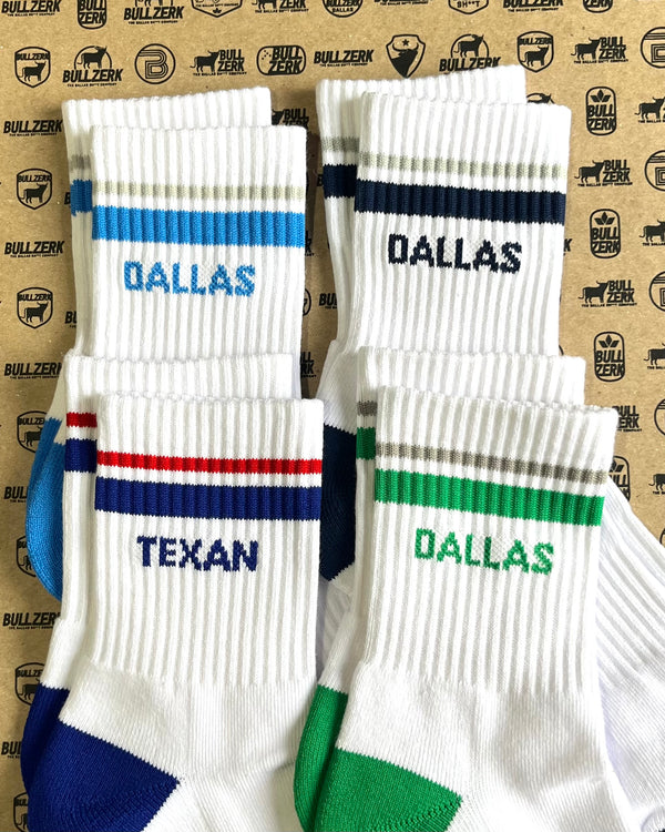 Four pairs of white socks with colored stripes and 'Dallas' and 'Texan' text on a branded background
