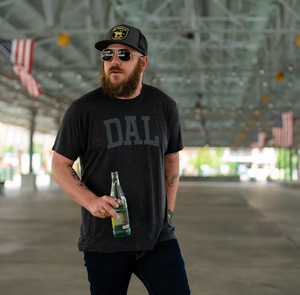 Photo of a man standing in a parking lot wearing sunglasses and the Bullzerk DAL Charcoal tshirt. 