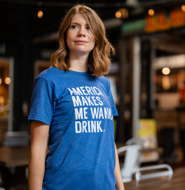 Photo of a woman standing in a food court wearing the Bullzerk America Makes me Wanna Drink tshirt. 