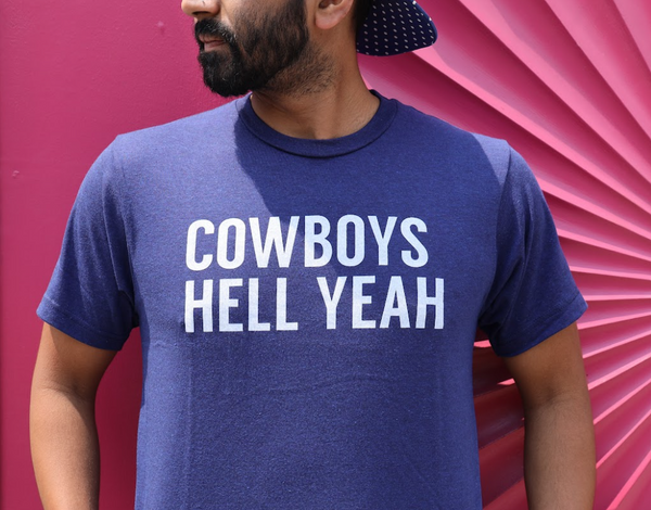Close up photo of a man wearing the Bullzerk Cowboys Hell Yeah tshirt in front of a pink wall. 