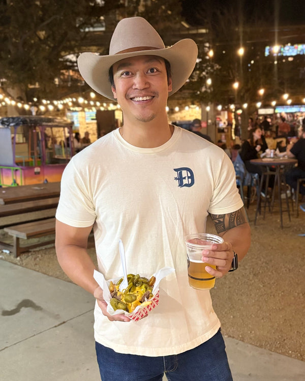 Man wearing a cowboy hat and a Bullzerk "D Spur" tshirt,  holding nachos and a beer in an outdoor setting.