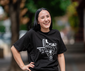 Woman standing outside and laughing, wearing a Bullzerk Icons of Dallas tshirt.