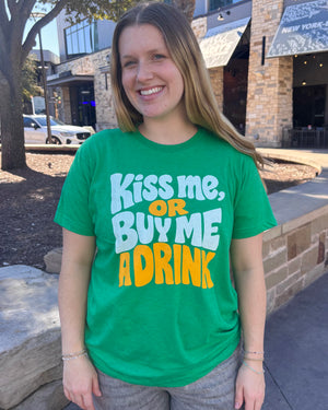 Woman wearing a Bullzerk Kiss Me Or Buy Me A Drink tshirt, standing outside. 