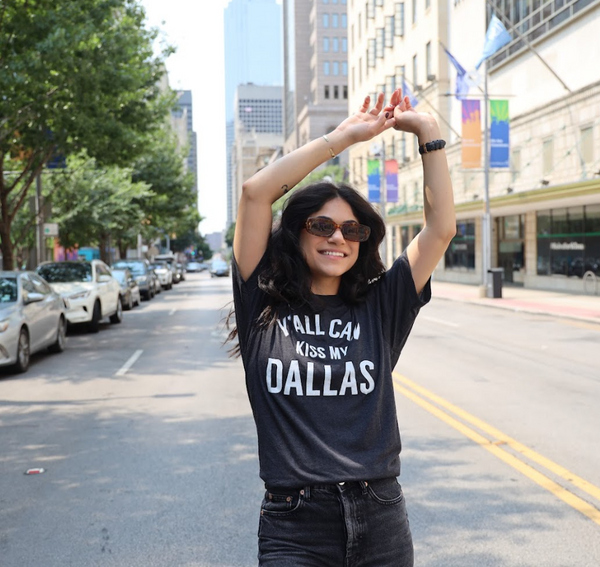 Woman wearing a Bullzerk "Y'ALL CAN KISS MY DALLAS" tshirt on a city street. 
