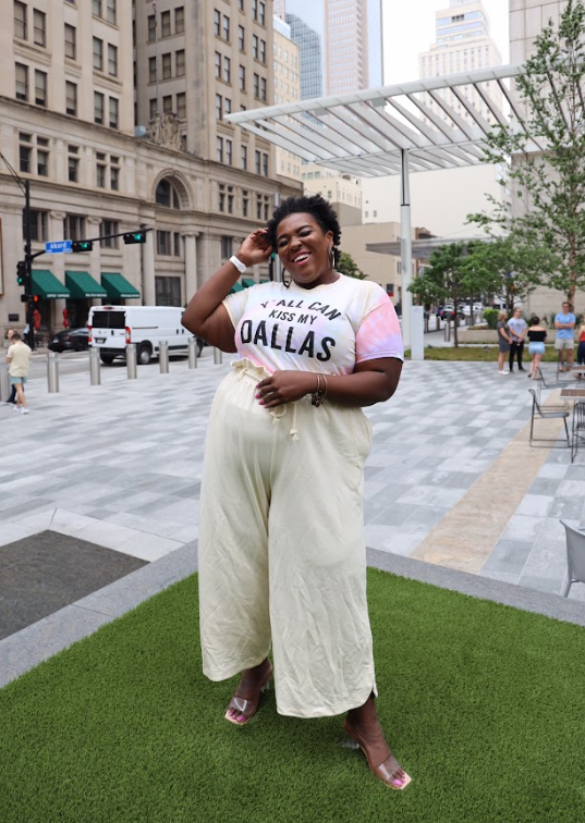 Woman standing in a park, laughing and wearing a Bullzerk Kiss My Dallas tie dye tshirt. 