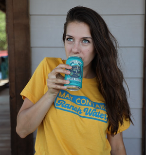Woman wearing a Bullzerk May Contain Ranch Water tshirt, drinking from a can of ranch water. 