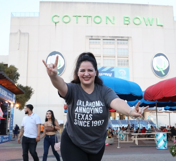 Woman in a Bullzerk 'Oklahoma Annoying Texas Since 1907' shirt posing in front of the Cotton Bowl.