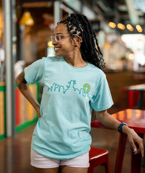Woman wearing a Bullzerk Skyline Plant tshirt, leaning on a table at the farmers market. 