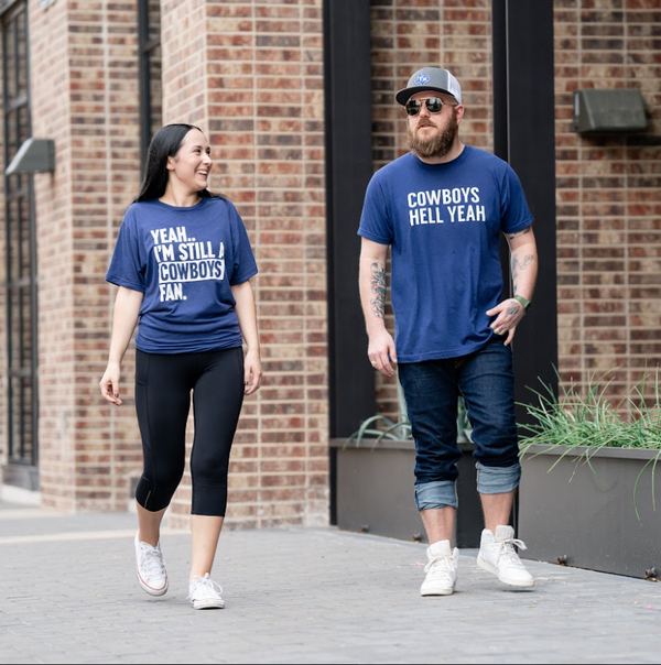 Two people wearing Bullzerk cowboys tshirts, walking down the sidewalk and talking. 