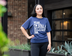 Woman wearing a Bullzerk Yeah I'm Still a Cowboys Fan tshirt, standing outdoors. 