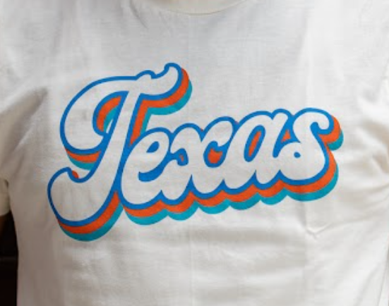 Cream t-shirt with 'Texas' printed in a script font in blue, orange and teal ink.