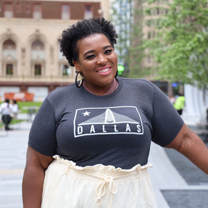 Woman wearing a Bullzerk Trinity t-shirt standing outdoors with buildings and trees in the background