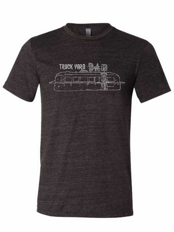 Dark, charcoal gray tshirt with graphic design of a metal trailer with a neon sign above it that reads "TRUCK YARD BAR." 